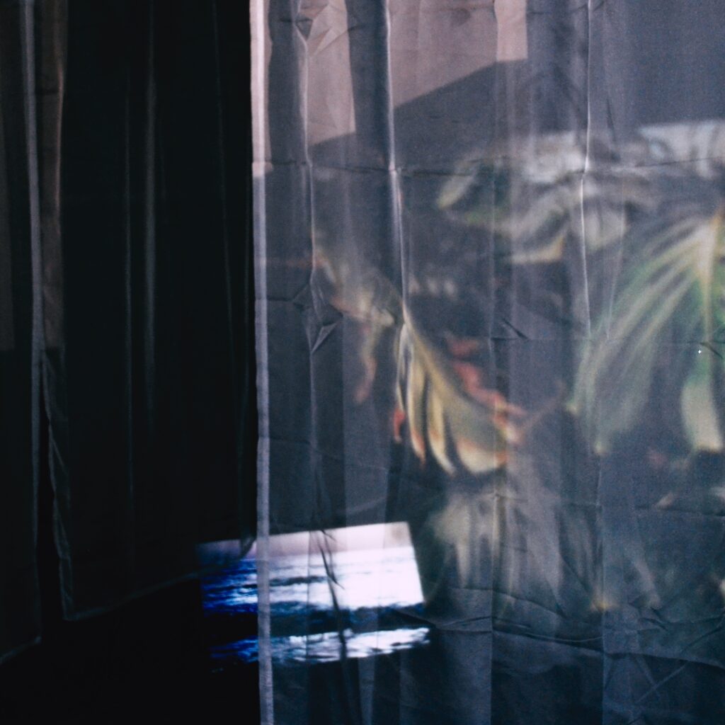 Cool-toned light installation with translucent fabric panels and soft reflective projections creating blurred organic shapes in a dim interior space.